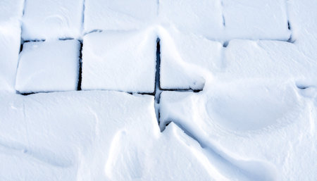 A thick blanket of fresh snow covers square paving stones, creating a textured, abstract pattern.の素材
