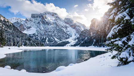 A picturesque winter vista of a snow-covered lake nestled among pine trees and rugged, snow-capped mountains.の素材