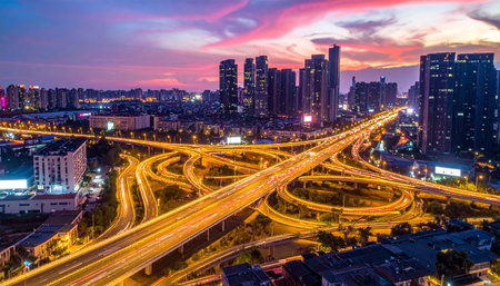 Aerial view of a multi-layered highway interchange at dusk, with glowing lights and a cityscape.の素材