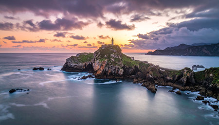 A lighthouse stands atop a rocky island at sunset with dramatic clouds and silky waterの素材