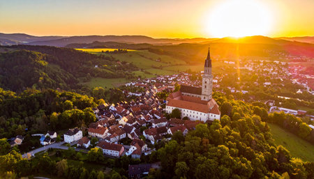 Drone view of a European monastery on a hill at sunset, overlooking a village and green landscape.の素材