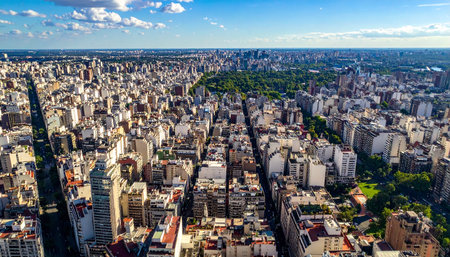 Expansive aerial view of a city with dense buildings surrounding a large green park under a blue sky.の素材