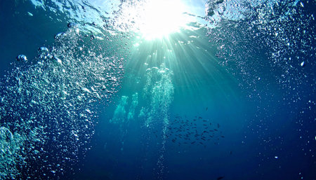 Sunbeams pierce deep blue ocean water with rising bubbles and a school of fish Clear details and vibrant colors enhan...の素材
