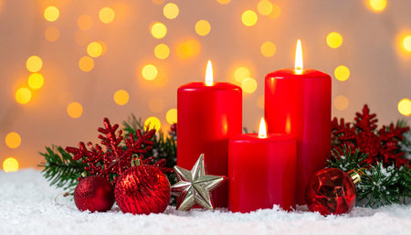 Four red advent candles glow amidst snow and festive Christmas decorations with bokeh lights.の素材