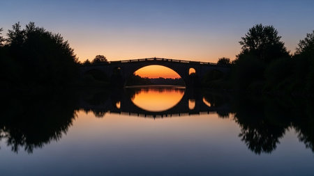 Sunset over the river with a bridge in the foreground and reflection in the waterの素材