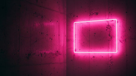 A sharp, rectangular outline of bright pink neon light emanates a vibrant glow against a dark, textured concrete wall. The rough surface of the concrete provides a gritty contrast to the clean, geometric lines of the neon sign. The light spills onto the wall, creating a soft halo effect. The scene is dark, with the neon light being the primary source of illumination, suggesting an urban or industrial setting, or a modern installation.の素材