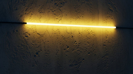 A single, bright yellow neon light tube stretches horizontally across a dark, rough-textured concrete wall. The light emits a warm, inviting glow that illuminates the uneven surface of the concrete, casting subtle shadows and highlighting its gritty texture. The stark contrast between the vibrant light and the dark, textured background creates a dramatic and atmospheric visual.の素材