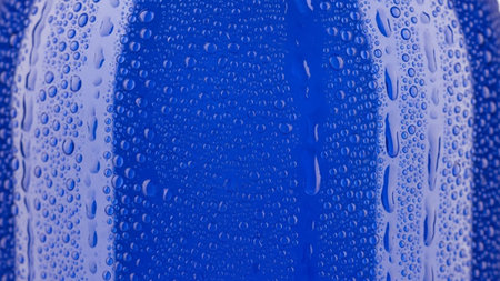An extreme close-up of a vibrant blue surface heavily covered in numerous small water droplets. The condensation creates a detailed, textured pattern of light reflecting off the wet surface. The conveys a sense of coolness, refreshment, and pristine cleanliness.の素材