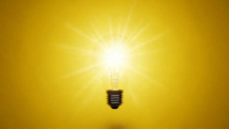 A single incandescent light bulb is prominently displayed against a vibrant, solid yellow background. The bulb is intensely bright, radiating a powerful burst of light outwards, creating a starburst effect. The filament inside the bulb is visible, and the metal base grounds the This composition is clean, minimalist, and symbolic, representing concepts such as ideas, innovation, creativity, and solutions. The intense light suggests brilliance and inspiration, making it a powerful visual metaphor.の素材