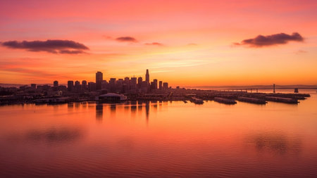 The San Francisco skyline is silhouetted against a vibrant sunset sky, painted with shades of pink and orange. The calm waters of the bay mirror the colorful sky and the city's impressive architecture. This aerial view captures the essence of the city at twilight, showcasing its unique charm and beauty. The wide panorama provides a sense of scale and grandeur, making it an for travel and city-themed projects.の素材