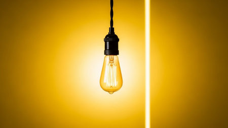 A solitary vintage Edison light bulb hangs suspended by a black cord against a vivid, gradient yellow background. The filament within the bulb glows with a warm, inviting light, casting a soft illumination. The contrast between the bright yellow backdrop and the dark cord emphasizes the simple elegance of the captures the essence of illumination, ideas, and retro with a clean, minimalist aesthetic.の素材