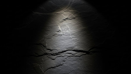 A dark slate stone surface with a bright spotlight highlighting intricate cracks and layers, creating dramatic...の素材