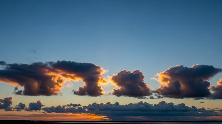 A serene sunset paints the sky with glowing orange clouds above a dark horizon and calm water.の素材