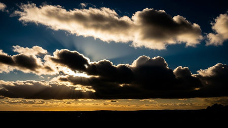 Silhouette showing dramatic sunset sky with dark storm clouds illuminated by golden sun rays breaking through the...の素材