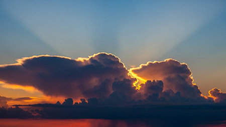 A dramatic sunset with golden sun rays piercing through dark clouds, illuminating a vibrant orange horizon above...の素材