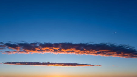 Textures showing vibrant orange clouds illuminated by sunset light against a deep blue sky with a distant contrail...の素材