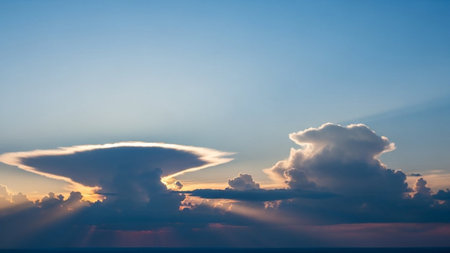 A dramatic sunset sky a lenticular cloud formation and cumulus clouds illuminated by visible sun rays breaking through.の素材