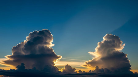 Towering cumulonimbus clouds are dramatically lit by golden sunset rays against a deep blue sky.の素材
