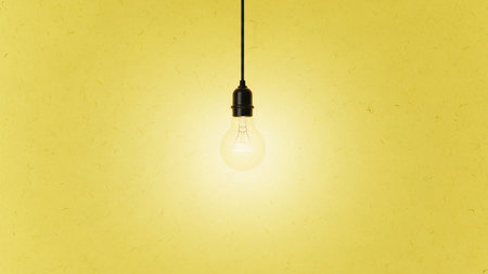 A single, lit incandescent light bulb hangs from a black cord against a textured yellow wall. The bulb emits a warm, bright glow that illuminates the immediate area. The background has a subtle, organic texture, adding depth and visual interest without distracting from the central The composition is minimalist and clean, focusing on the simple form of the light bulb and its radiant light.の素材