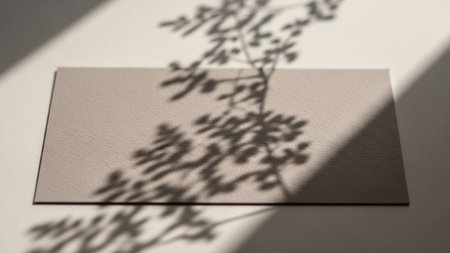 Soft, dappled shadows of delicate plant leaves and branches are cast across a subtly textured beige surface. The natural light creates a gentle, ephemeral pattern, highlighting the organic shapes and intricate details of the foliage. This minimalist composition evokes a sense of tranquility and natural beauty, creating a serene and atmosphere.の素材