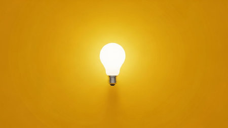 A single, classic incandescent light bulb is prominently displayed, emitting a bright, warm white glow. It is positioned centrally against a solid, vibrant yellow background, creating a stark contrast. The light from the bulb casts a subtle shadow beneath it, adding a sense of depth. The is clean, minimalist, and focuses entirely on the illuminated making it a strong visual representation of ideas, innovation, or energy. The overall impression is one of simplicity and focused brilliance.の素材