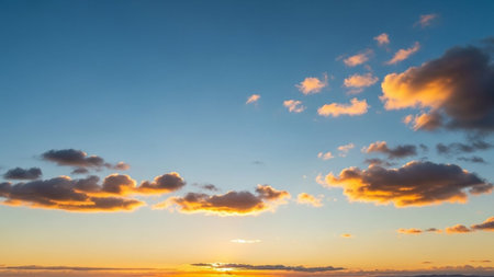 Yellow showing vibrant sunset sky with golden orange and yellow hues illuminating fluffy clouds against a clear blue...の素材