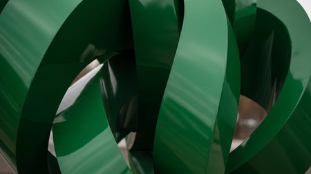 A close-up view of a glossy metallic green abstract sculpture featuring swirling, curved ribbons that create a...の素材