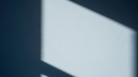 A soft blue textured wall a sharp geometric shadow from window light, creating a minimalist abstract pattern.の素材