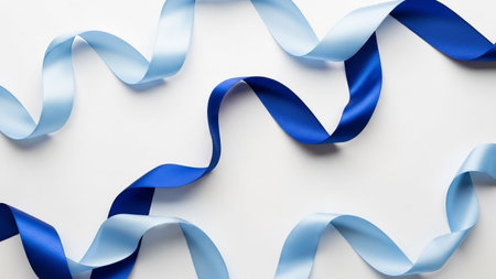 Two satin ribbons, one light blue and one dark blue, flow and curl elegantly across a plain white background.の素材