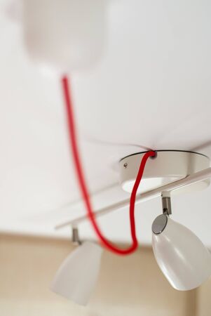 White lamp with two spotlights with red cable on white ceiling