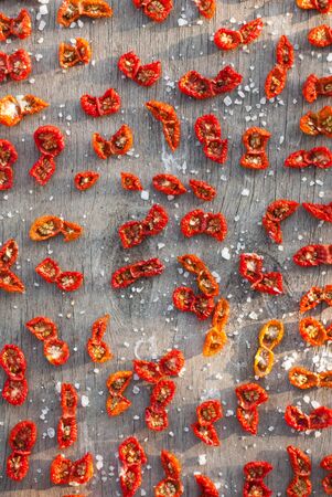Top view of a wooden table filled with dried tomato slices and grains of coarse salt