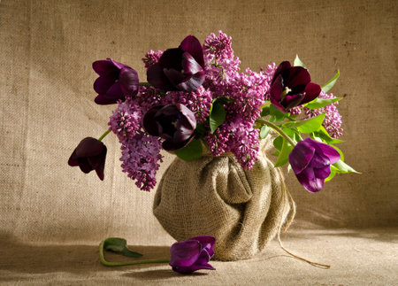 Beautiful bouquet of tulips with sprigs of lilac in a vase on a burlap backgroundの写真素材