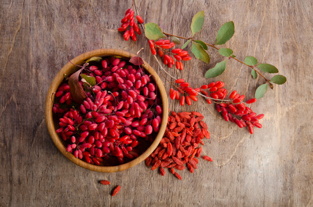 Barberry in bowl with leaves and dry goji berries on wooden backgroundの写真素材