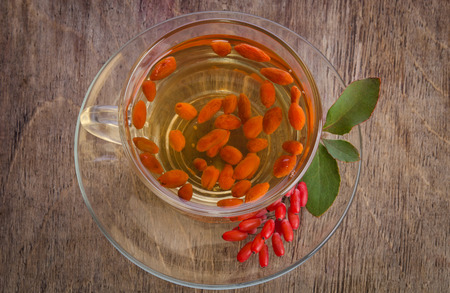 goji fresh antioxidant tea in glass cup and barberries in wooden desk. studio photo top viewの写真素材
