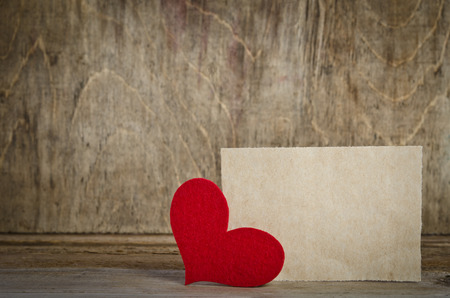 Red fabric heart with sheet of paper standing on a wooden board. On old wood background.の写真素材