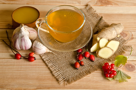Cup of tea,slices of ginger,honey,rosehip berries and viburnum on a wooden tableの写真素材