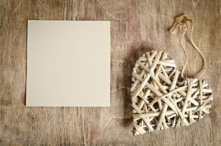 wicker heart handmade lying on a wooden base with a sheet of paperの写真素材