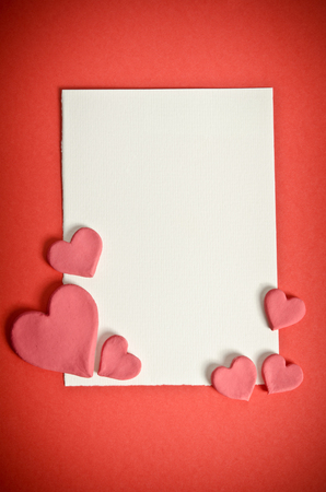 white paper with small pink hearts lying on a red backgroundの写真素材