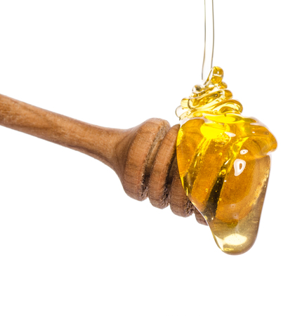 Honey dripping from a wooden honey dipper isolated on white backgroundの写真素材
