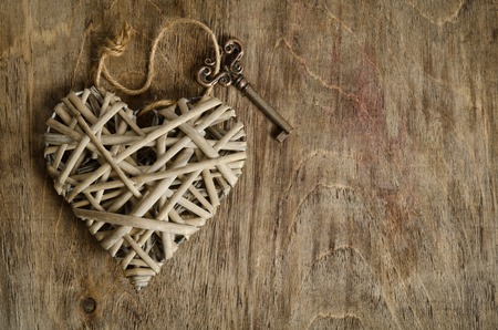 wicker heart handmade with the key lying on a wooden base . top viewの写真素材