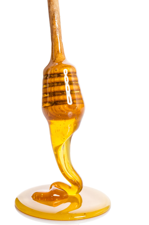 Honey dripping from a wooden honey dipper on white backgroundの写真素材