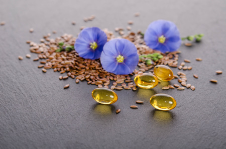 Flax seeds , beauty flower and oil in caps on a grey background. Phytotherapy.の写真素材