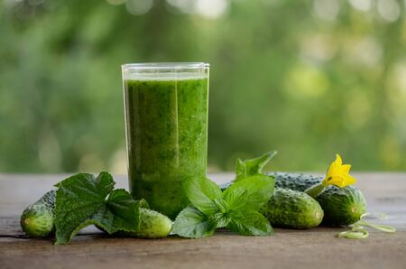  glass with green smoothie on a wooden table and  cucumbers with flowers and mint leavesの写真素材