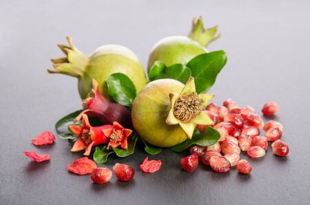 Three green pomegranates with seeds and leaves with petals on grey backgroundの写真素材