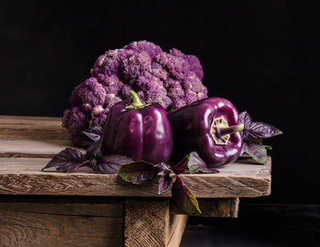 Fresh vegetable. Dark purple peppers, cauliflower with leaves of basil  on old rustic wooden table on black backgroundの写真素材