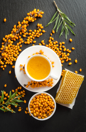 Sea buckthorn, honeycomb with honey and cup of  tea on black stone table.の写真素材