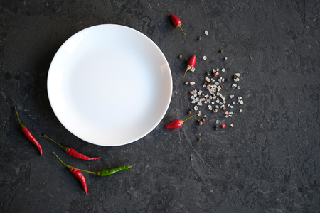 White plate on black stone background. Hot chilli pepper, salt and spices around the plateの写真素材