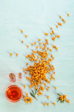 Sea buckthorn with two bottles  and bowl with sea buckthorn oil  on blue tableの写真素材
