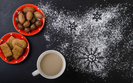 On a black top, a saucer of cookies and a saucer of nuts and a cup of cocoa. Christmas decoration.