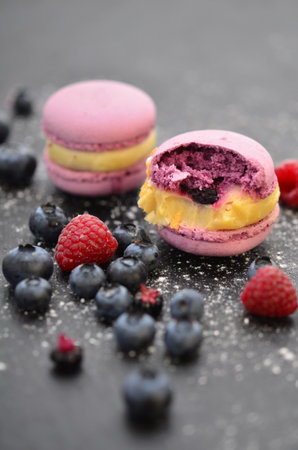 Delicious macaroons and berries on a black tray. Raspberries and blueberries are juicy berries. treat.の写真素材
